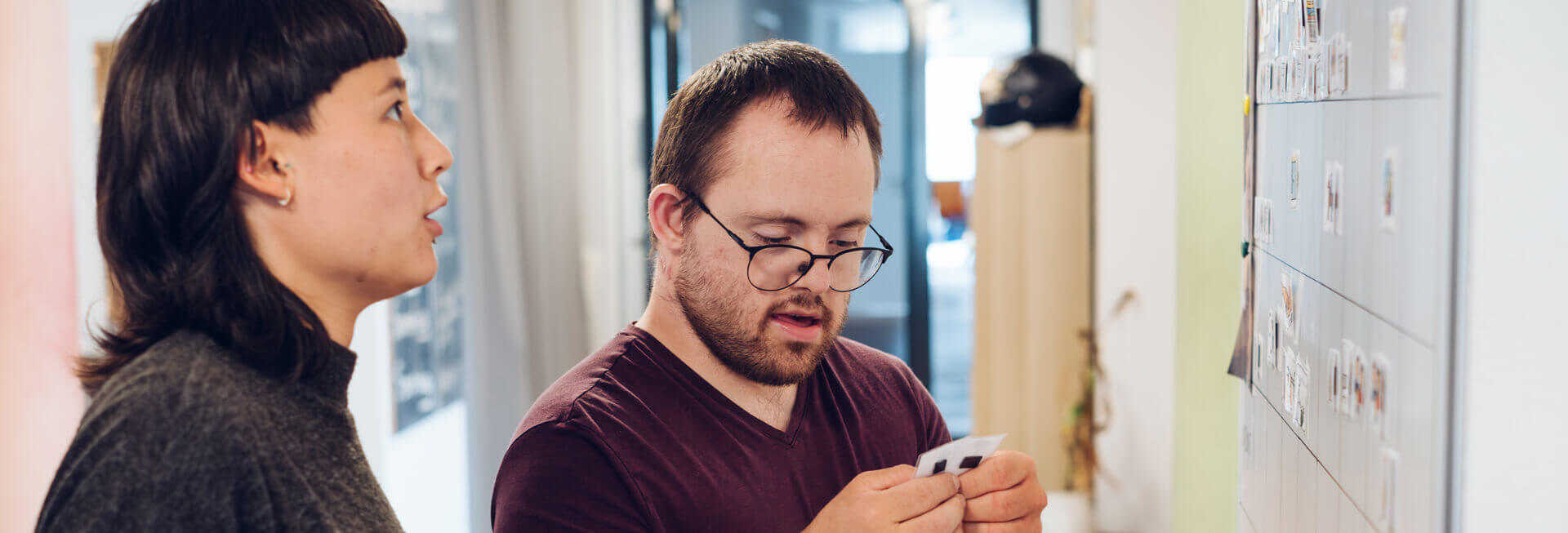 Ein Junge und ein Mädchen, mit und ohne Behinderung, stehen vor einer Tafel und planen die Vorgänge und Aufgaben in der inklusiven WG.
